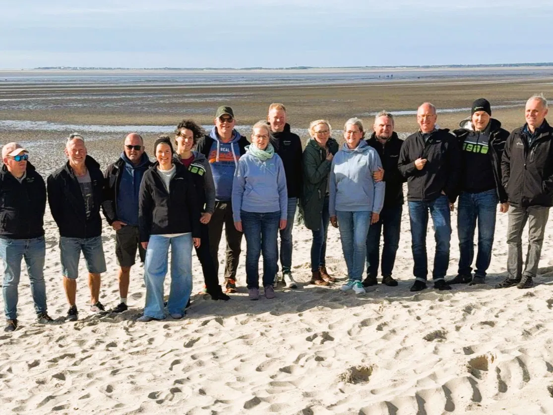 Gruppenbild von 14 Mitarbeitenden vor dem Wattenmeer am Strand